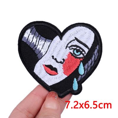 Heart-shaped patch with a face design held by a hand, on a white background.