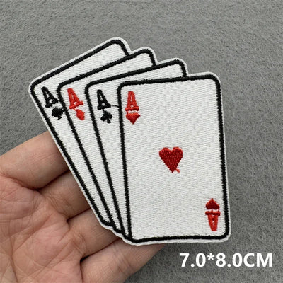 Embroidered patch of four aces on playing cards held by a hand against a gray background.