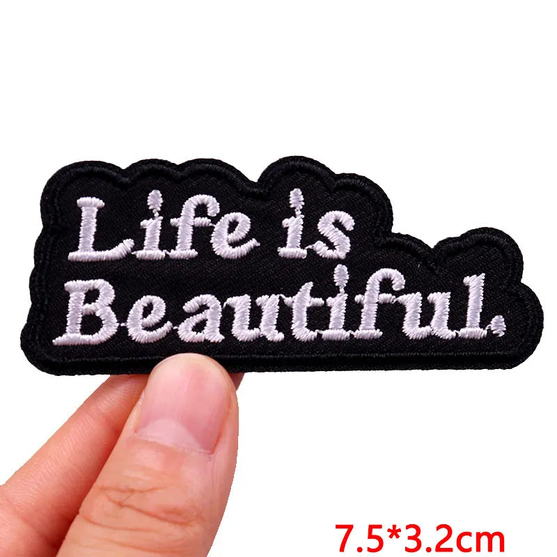 Black patch with 'Life is Beautiful' text held by a hand on a white background