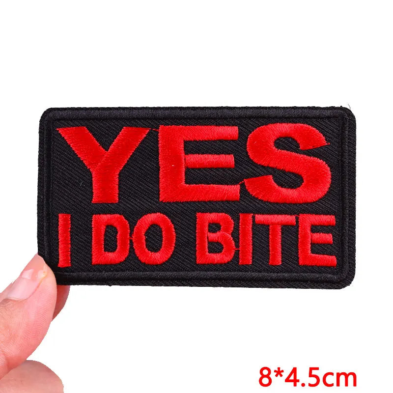 Embroidered patch with 'YES I DO BITE' text held by a hand, on a white background.