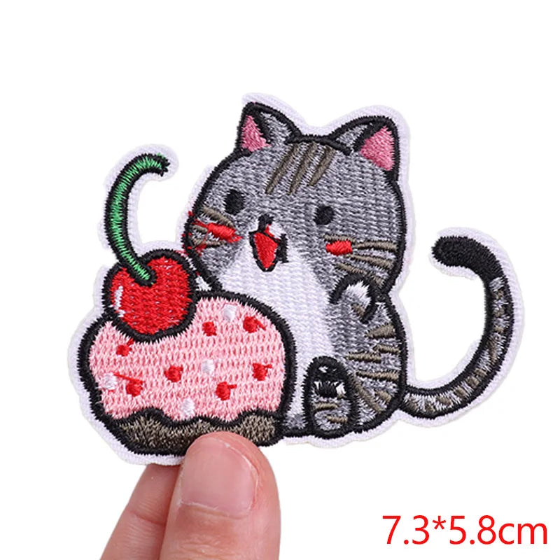 Embroidered patch of a cat with a cherry, held by a hand on a white background.