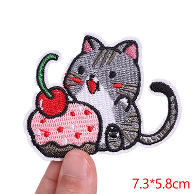 Embroidered patch of a cat with a cherry, held by a hand on a white background.