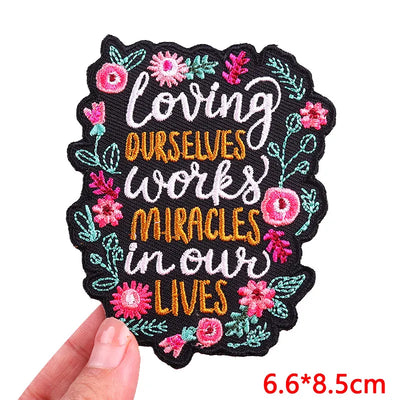 Embroidered patch with motivational quote and floral designs held by a hand on a white background.