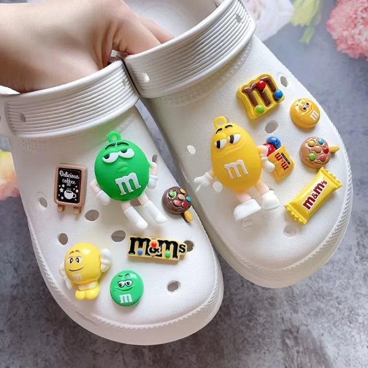 White clogs with colorful M&amp;M-themed charms on a gray surface