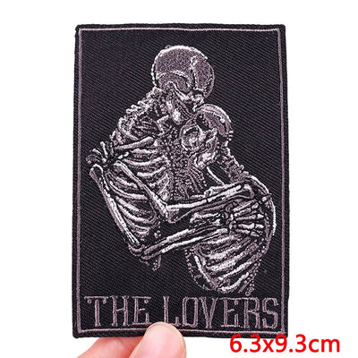 Patch with skeleton design labeled 'The Lovers' held by a hand on a white background