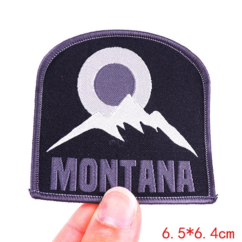 Patch with mountain design and 'Montana' text held by a hand on a white background