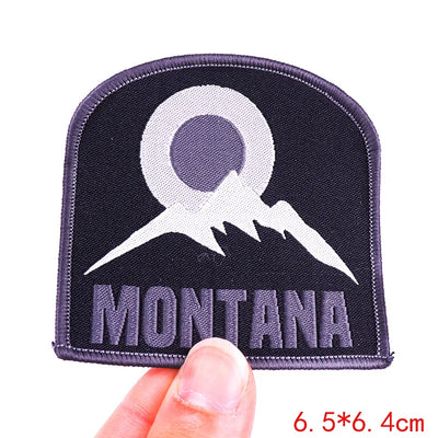 Patch with mountain design and 'Montana' text held by a hand on a white background