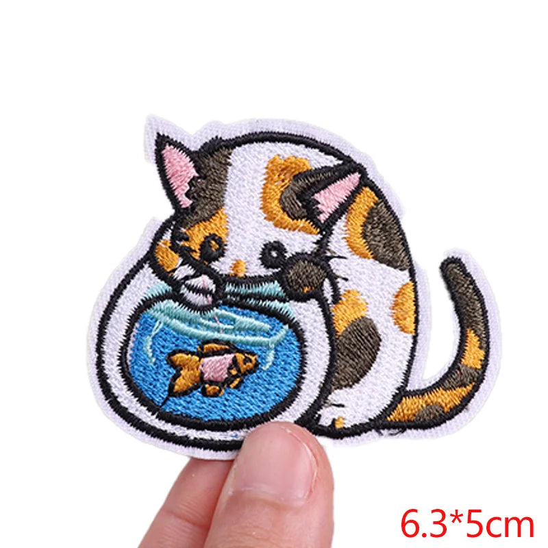 Embroidered patch of a cat with a fishbowl held by a finger, on a white background.