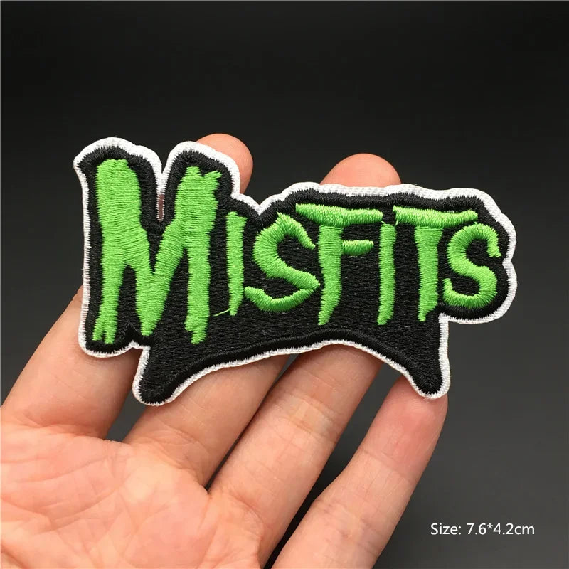 Hand holding a green and black Misfits embroidered iron-on patch 7.6x4.2cm on a dark background