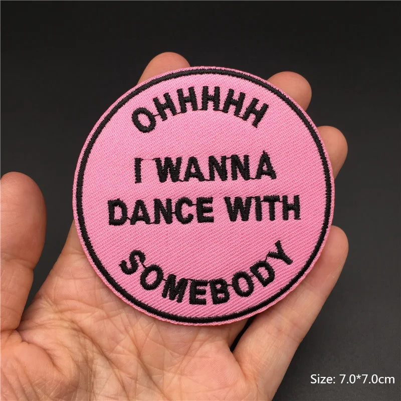 Pink patch with black text held in a hand against a dark background