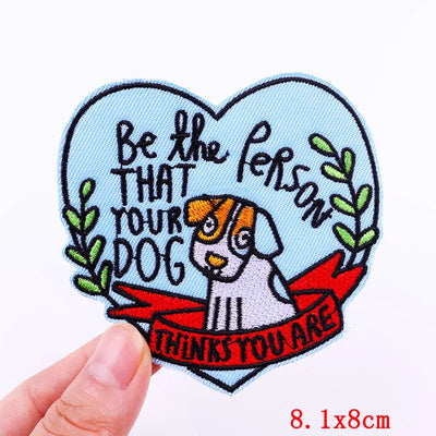 Heart-shaped patch with a dog illustration and text held by a hand on a white background