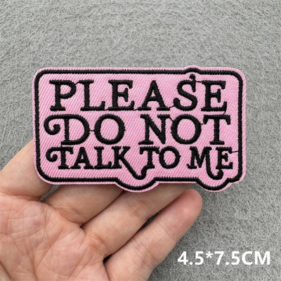 Pink patch with 'Please do not talk to me' text held in a hand against a gray background