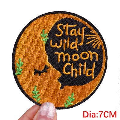Circular patch with 'Stay wild moon Child' text on a brown background, held by a hand.