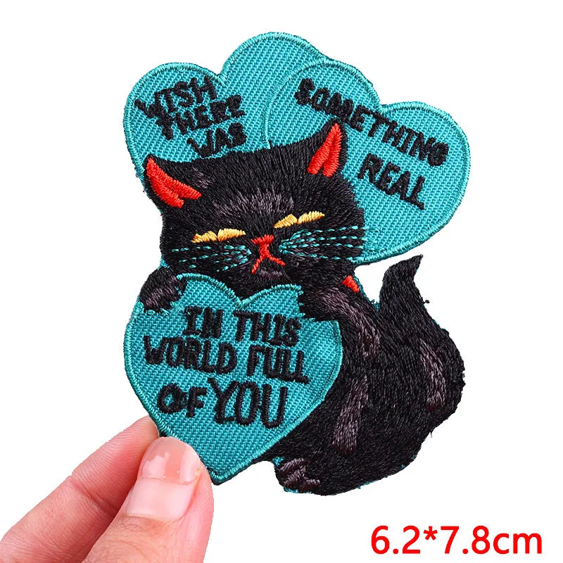 Embroidered patch with a black cat holding a heart, text, and a hand holding it.