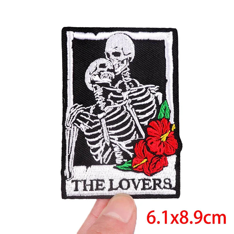 Patch with skeletons embracing and red flowers labeled 'The Lovers' held by a hand.