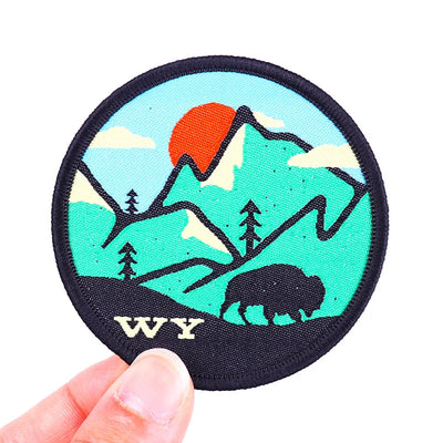 Round patch with mountain and bear design, featuring 'WY' text, held by a hand on a white background.