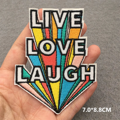 Colorful patch with 'Live Love Laugh' text held in a hand against a gray background