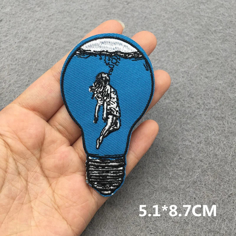 Embroidered patch of a person in a light bulb held between fingers on a gray background