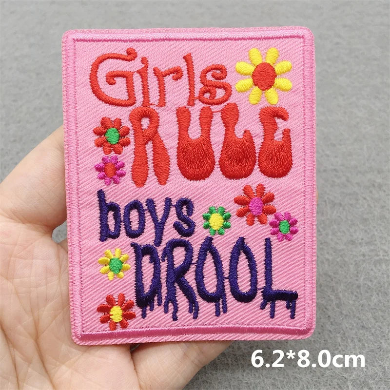 Embroidered patch with 'Girls Rule, Boys Drool' text held in a hand against a gray background.