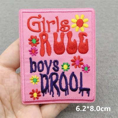 Embroidered patch with 'Girls Rule, Boys Drool' text held in a hand against a gray background.