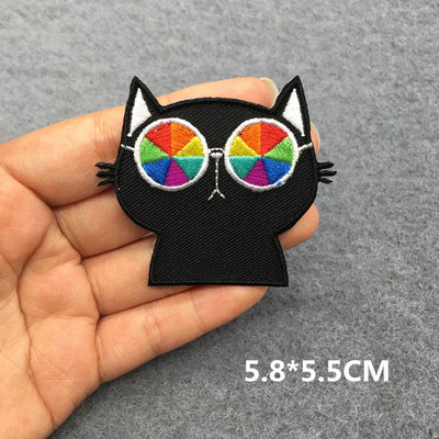 Black cat-shaped patch with rainbow sunglasses held in a hand on a gray background