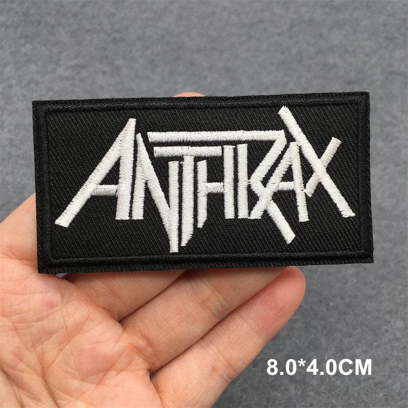 Hand holding a black and white Anthrax embroidered iron-on patch 8x4cm on a grey background