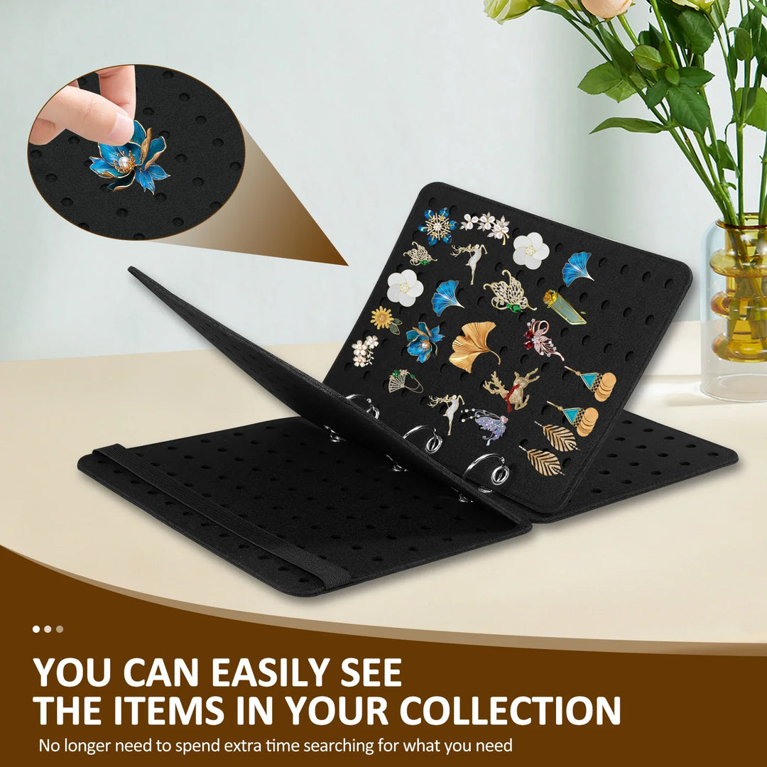 Black jewelry display folder with various brooches on a table with flowers in the background