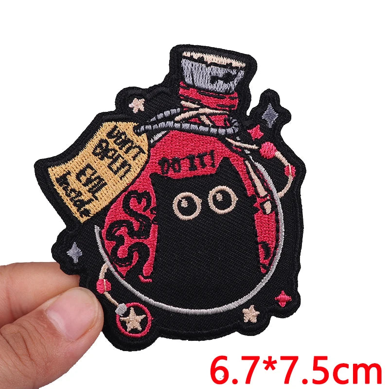 Embroidered patch with a black cat design held by a hand, on a white background.