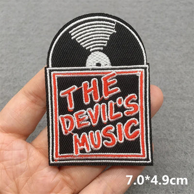 Patch with 'The Devil's Music' text held in a hand against a gray background