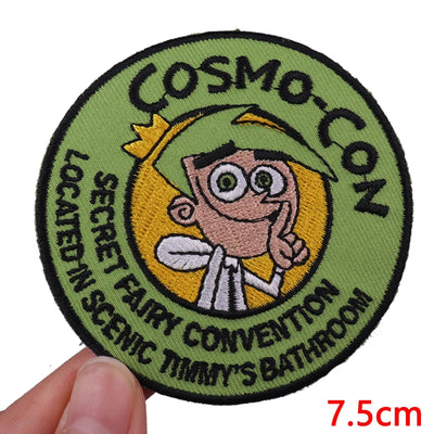 Circular patch with cartoon character and text 'Cosmo Con' held by a hand.
