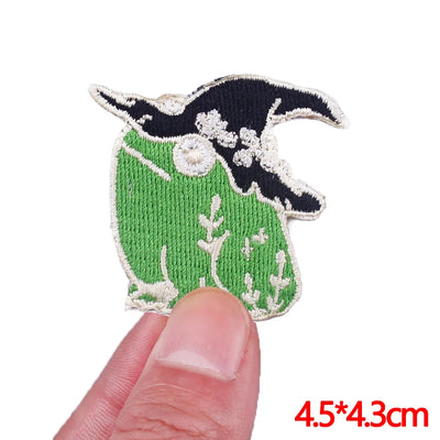 Embroidered patch of a green and black design held by a finger, with dimensions displayed.