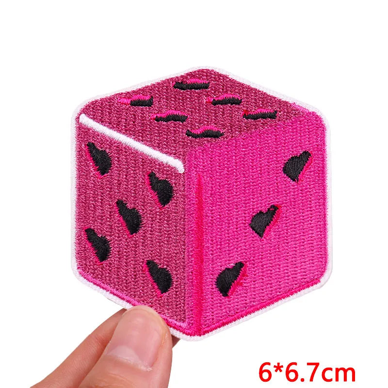 Pink dice-shaped patch with black details held by a hand on a white background