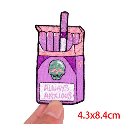 Patch of a pink cigarette pack with a skull and 'Always Anxious' text, held by a hand.