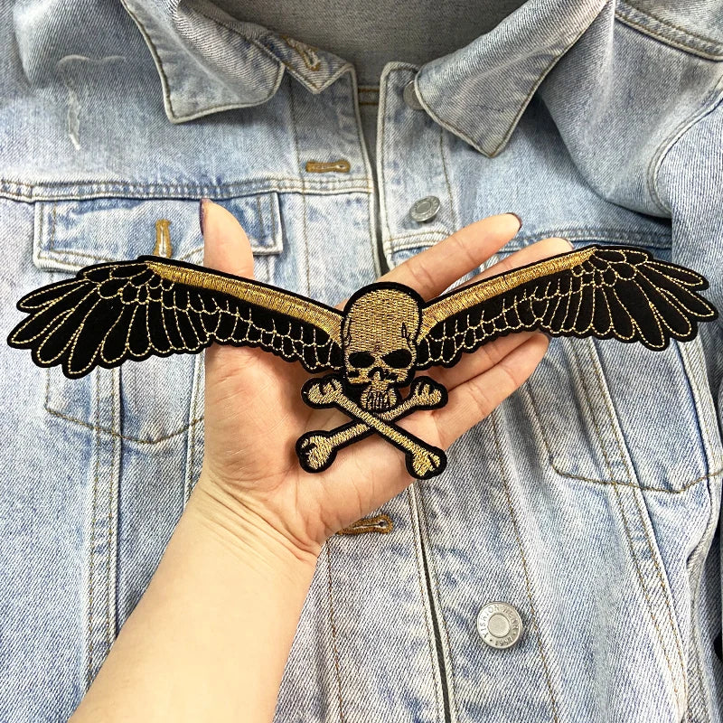 Hand holding a skull and wings patch against a denim jacket background