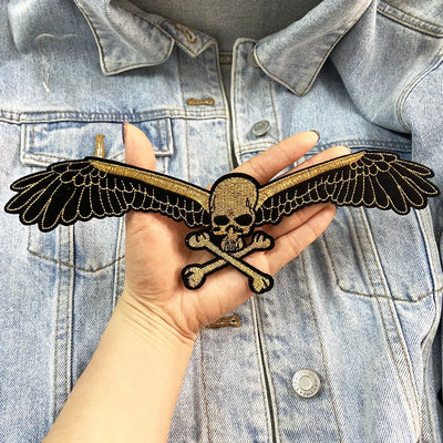 Hand holding a skull and wings patch against a denim jacket background