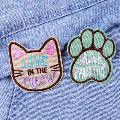 Two patches on a denim jacket: one with a cat face and 'Live in the meow' text, the other with a paw print and 'Think Positive' text.