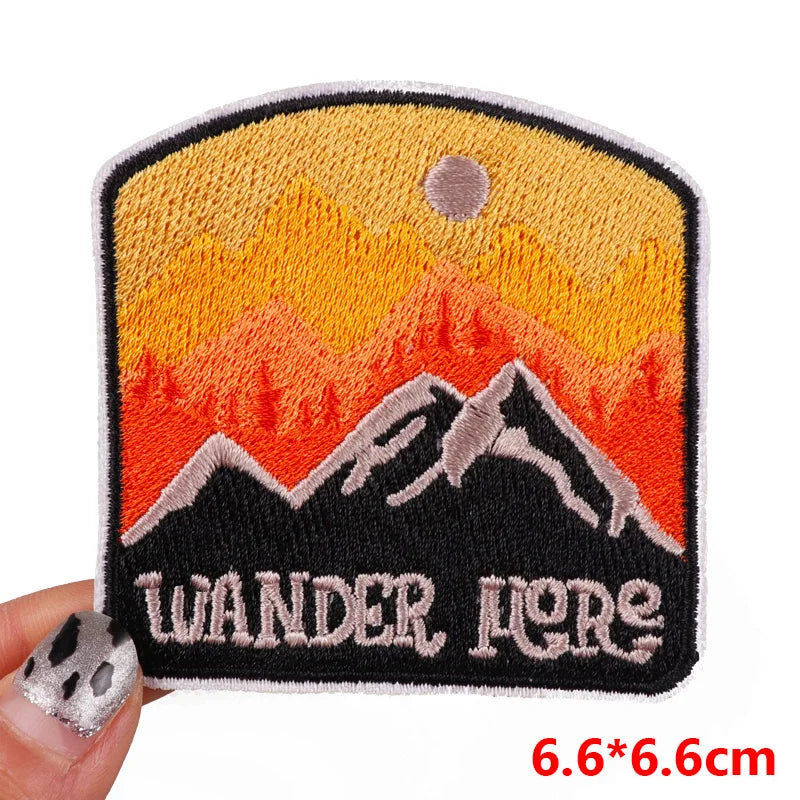 Embroidered patch with mountain design and 'Wander More' text held by a hand.