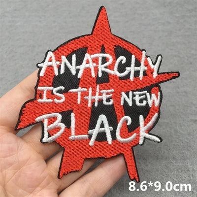 Embroidered patch with 'Anarchy is the New Black' text held in a hand against a gray background.