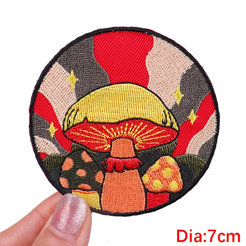 Circular embroidered patch with mushrooms held by a hand, on a white background.