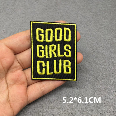 Patch with 'GOOD GIRLS CLUB' text held in a hand on a gray background