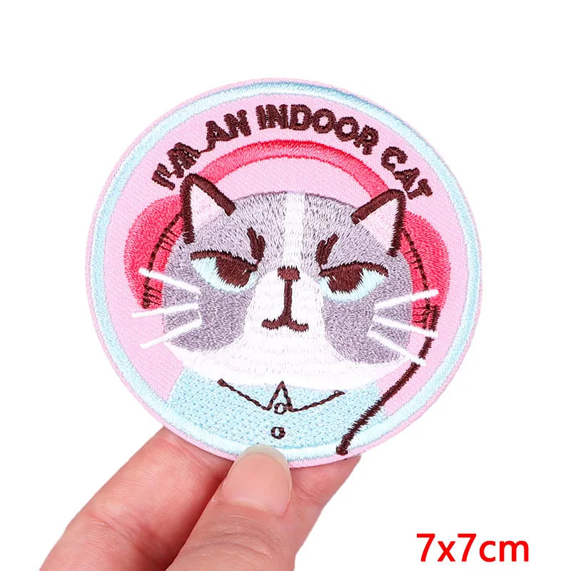 Circular patch with a cat design and text held by a hand on a white background