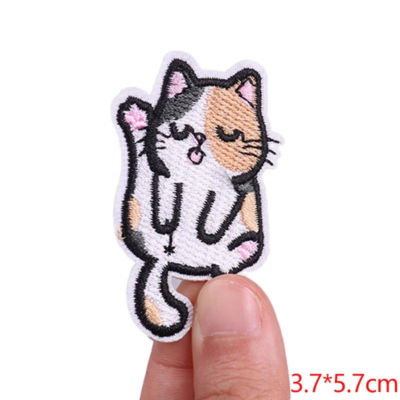 Embroidered patch of a cat design held between fingers on a white background