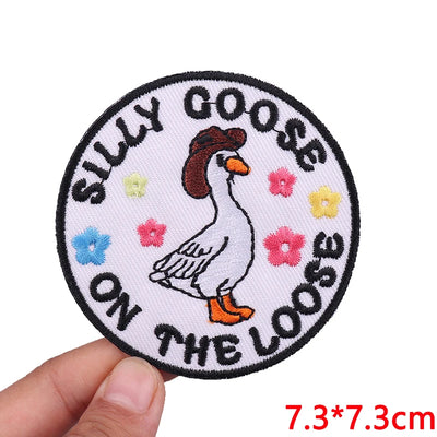 Circular patch with a goose illustration and text held by a hand on a white background