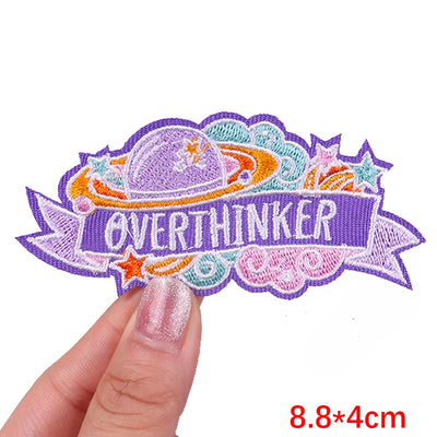 Embroidered patch with 'OVERTHINKER' text held by a hand on a white background