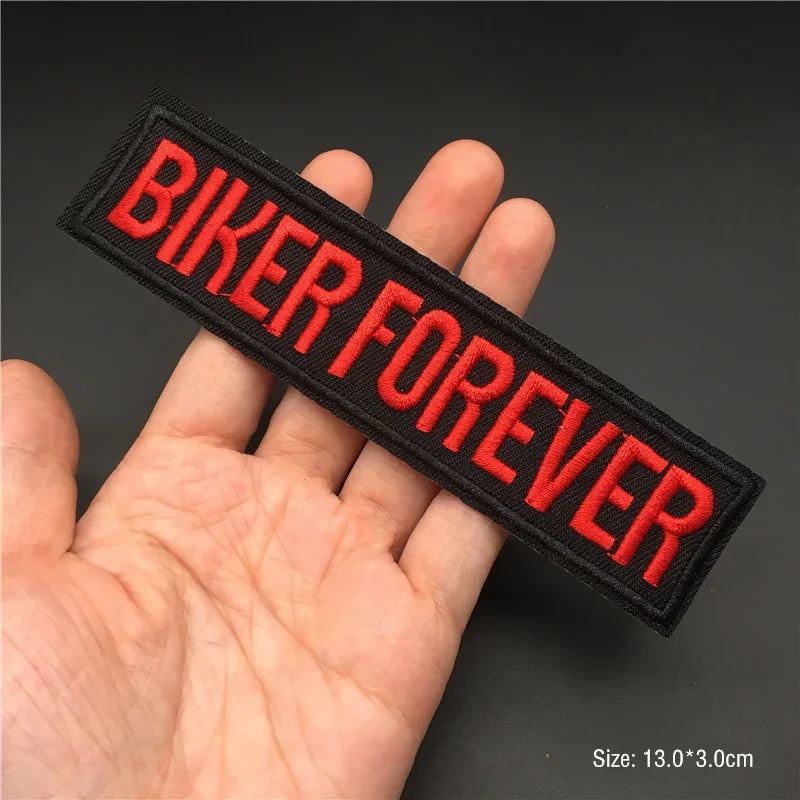 Hand holding a black and red BIKER FOREVER embroidered iron-on patch 13x3cm on a dark background