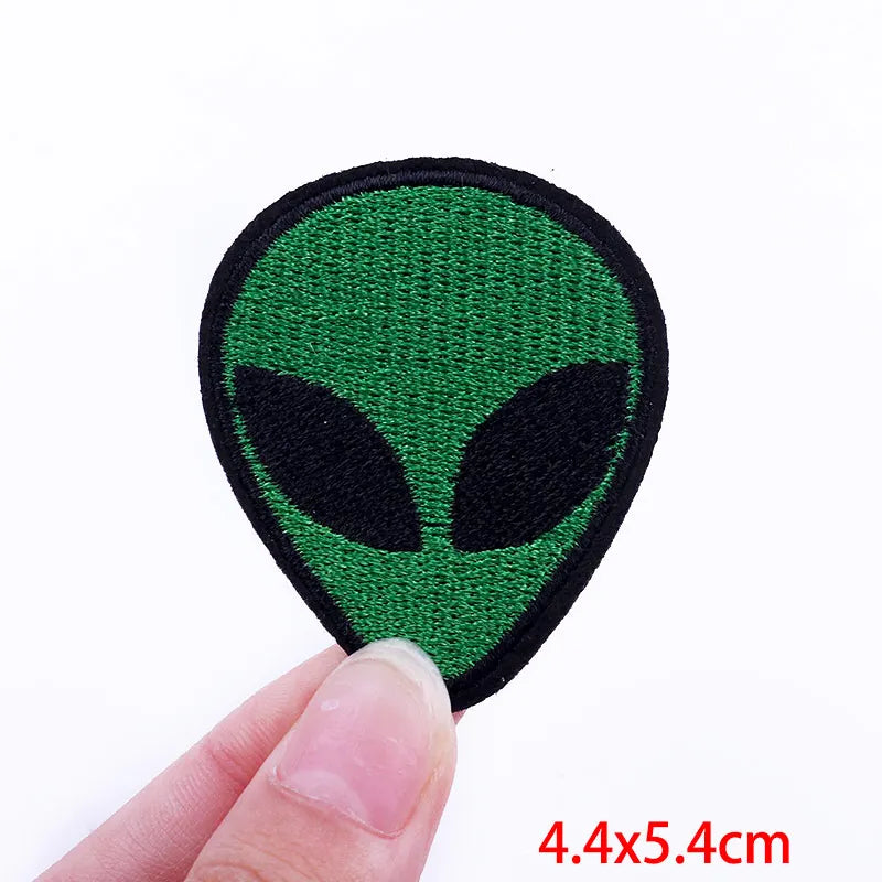 Green alien patch held by a hand with size label '4.4x5.4cm' on a white background