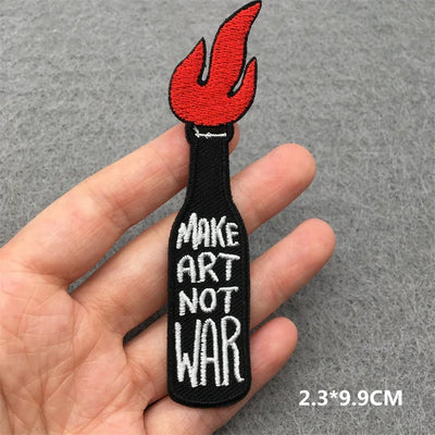 Embroidered patch with 'Make Art Not War' text held in a hand on a gray background