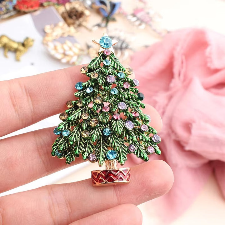 Decorative Christmas tree brooch with gemstones held in a hand against a blurred background.