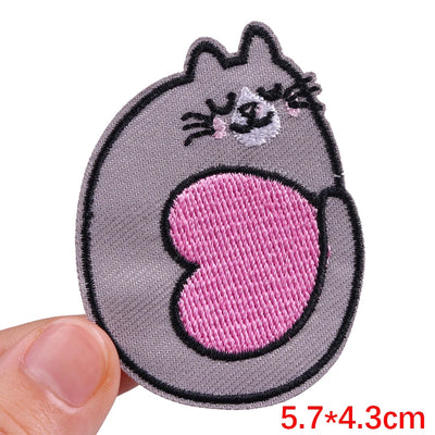 Embroidered patch of a cat with a pink heart on a gray background, held by a hand.