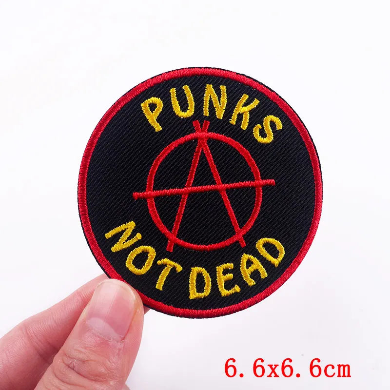 Patch with 'Punks Not Dead' text and anarchy symbol held by a hand on a white background.